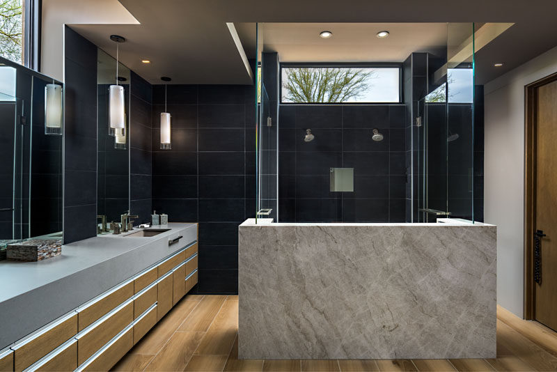 In this modern master bathroom, dark tiles cover the walls, while a walk-in two-person shower draws attention from anyone walking into the bathroom. #BathroomDesign #ModernBathroom