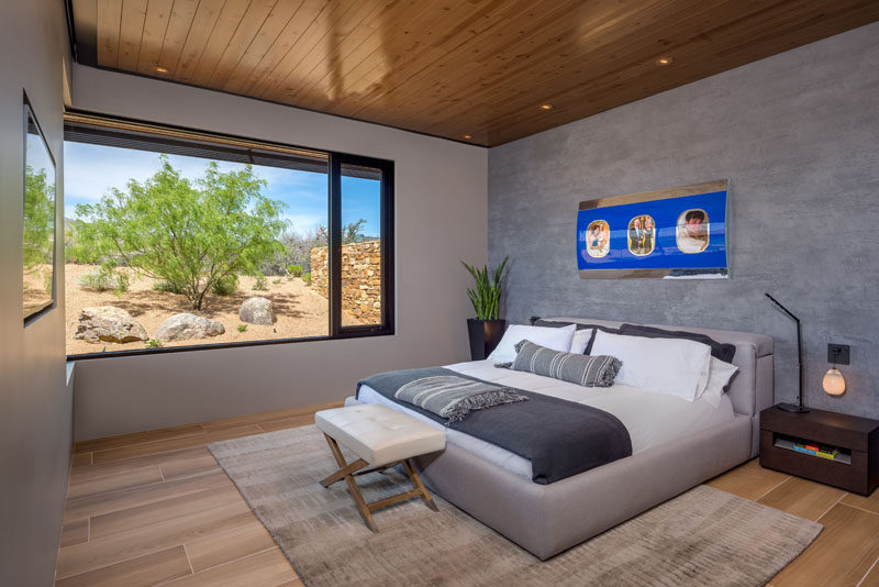 In this modern bedroom, a grey accent wall creates a calming atmosphere, while the windows perfectly frame the trees outside. #BedroomDesign #ModernBedroom #Windows