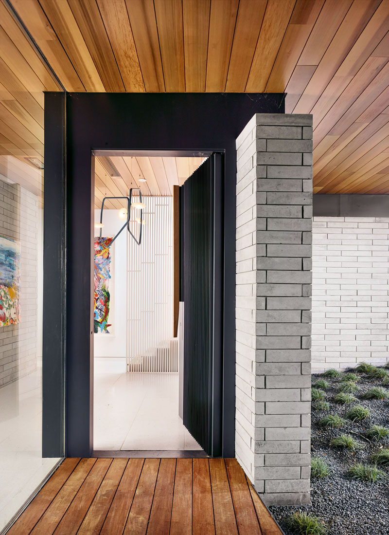 This modern house has a black front door that contrasts the wood ceiling and deck, and the white interior floors. #BlackFrontDoor #Door