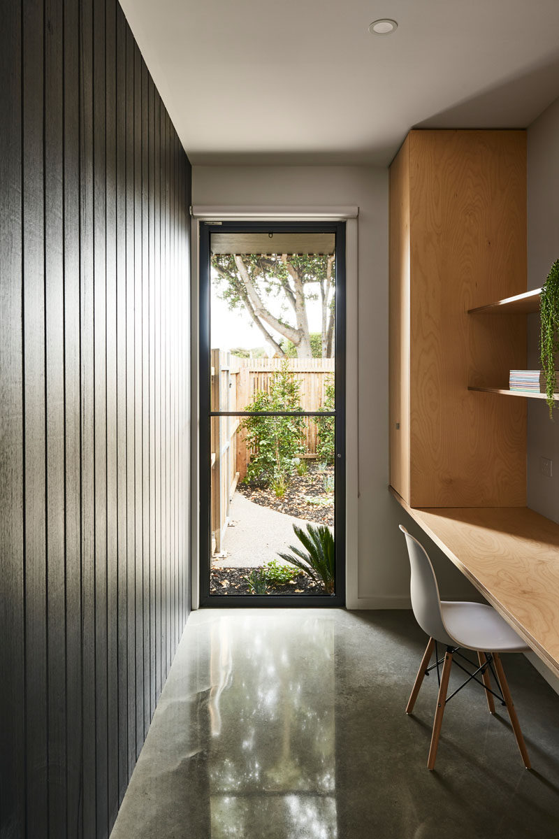 This modern home office with a polished concrete floor, features a black-stained wood accent wall, and a desk made from plywood. #HomeOffice #ConcreteFloor