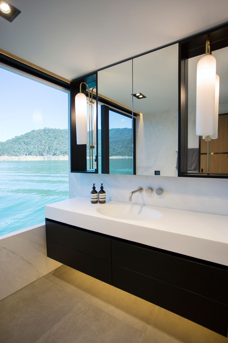 In this modern houseboat bathroom, the dark floating cabinetry of the vanity contrasts the seamless white countertop. #BathroomDesign #ModernBathroom