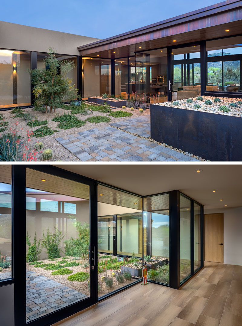 A small courtyard with a simple garden, steel planter boxes, and a stone path, leads to the glass front door of this modern house. #Landscaping #GlassWalls #GlassFrontDoor