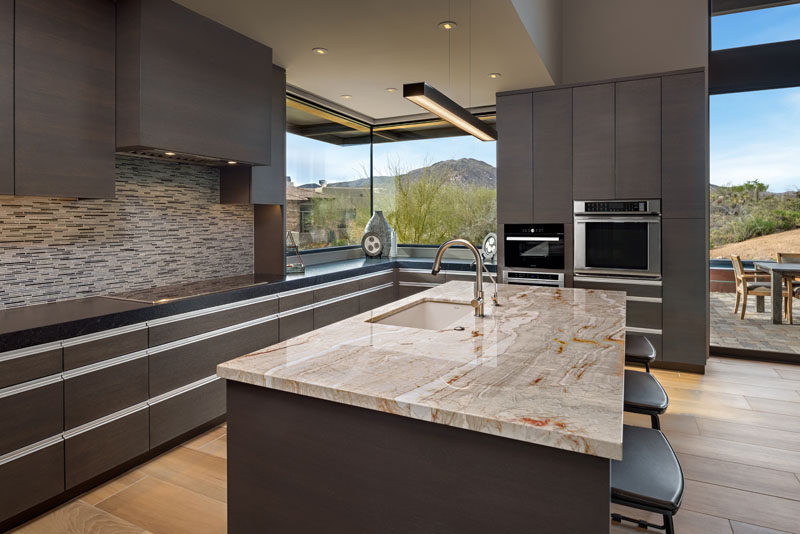 In the this modern kitchen, dark cabinetry is combined with earth-tone tiles and stone countertops to create a contemporary appearance. #ModernKitchen #DarkCabinetry