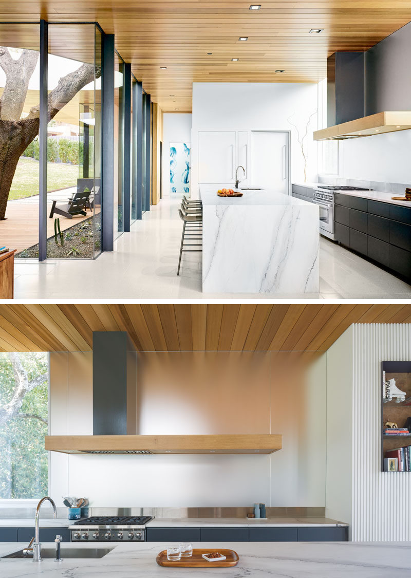 In this modern kitchen, dark cabinets and a metallic backsplash contrast the light countertops. #ModernKitchen #KitchenDesign #WoodCeiling