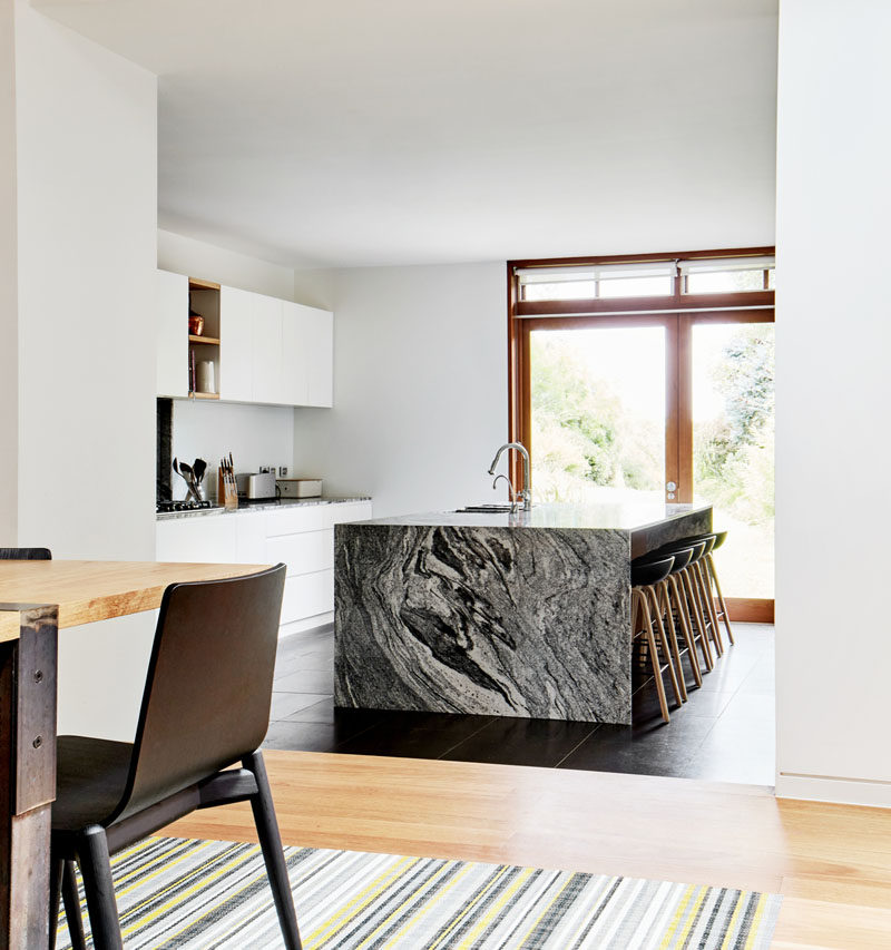 This modern kitchen has a large grey/black island with seating, while wood accents and door frames add a natural touch to the interior. #Kitchen #ModernKitchen #KitchenDesign