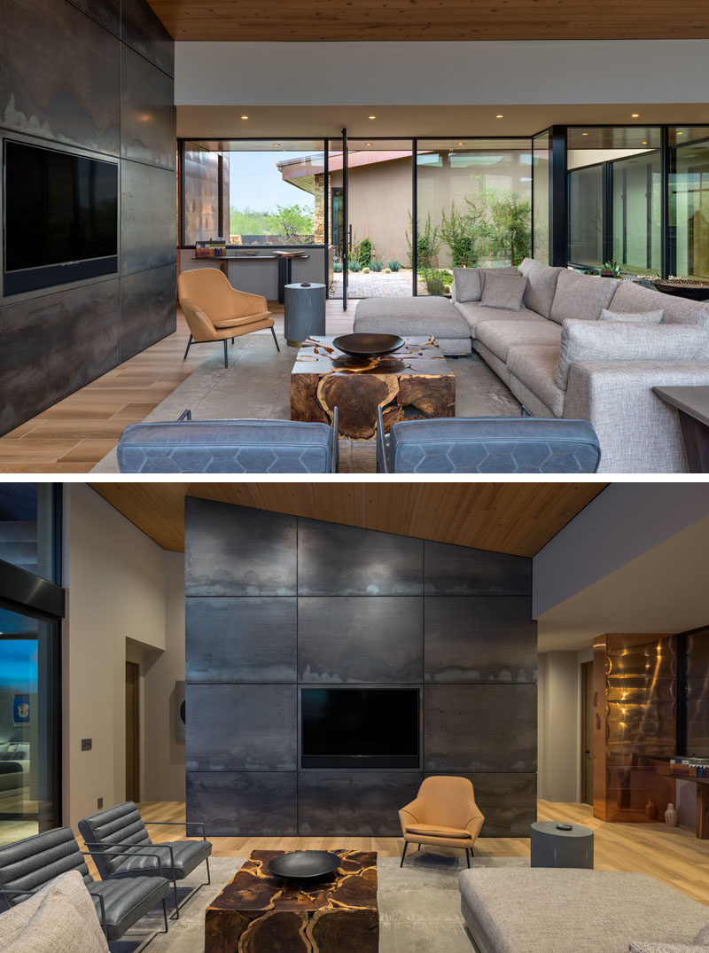 The front door of this modern house opens to the living room, that features a large steel accent wall. Walls of glass provide daylight to the interior and frame the garden and views outside. #ModernLivingRoom #SteelAccentWall #GlassWalls