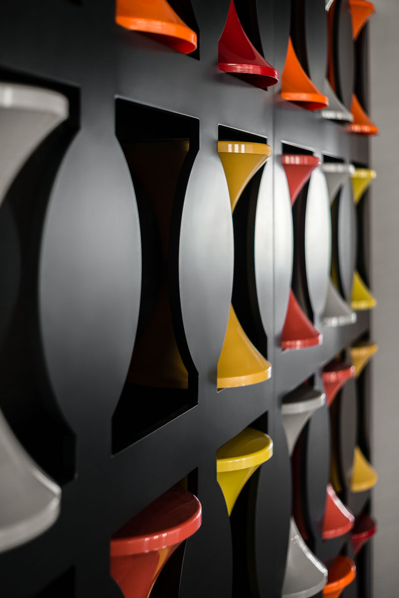 This modern office has a wall with cut-outs, that's dedicated to the storage of hourglass stools. When the stools aren't in use, they are placed into the empty spots in the wall, creating more room for walking around. #Stools #OfficeDesign #Workplace #WallStorage