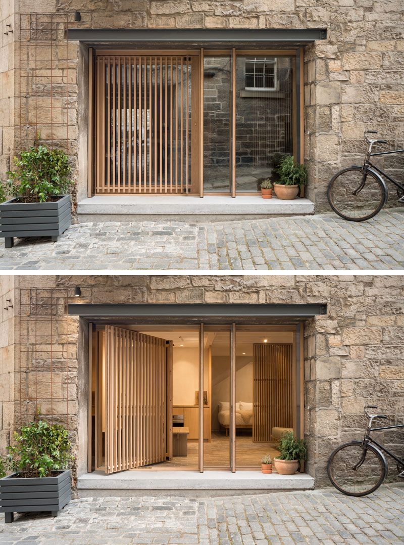 The original opening of this old blacksmiths shop was repurposed with deep mullioned windows and a wood screened pivot door, providing both privacy and views of the courtyard. #PivotingDoor #WoodSlatDoor #Windows