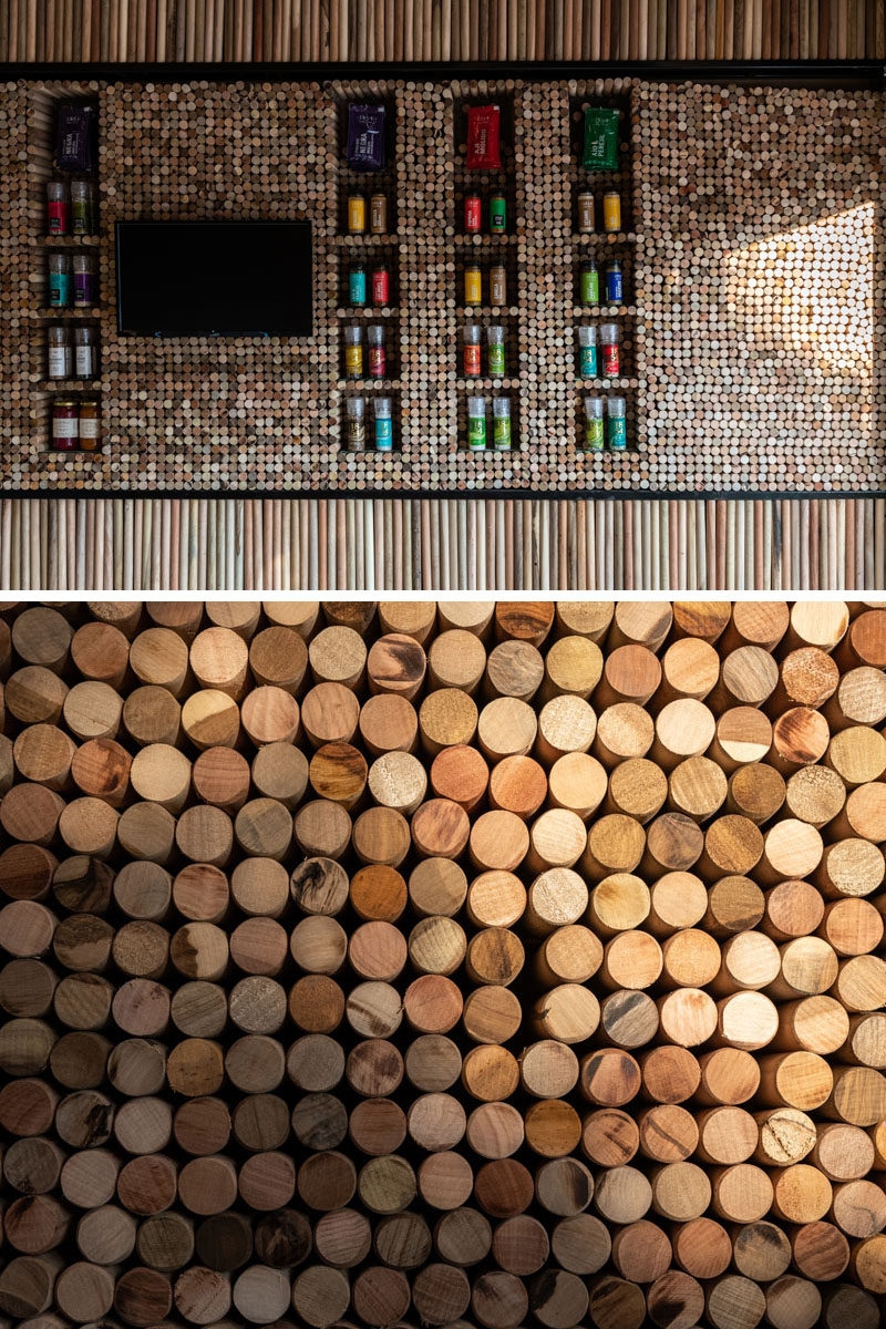 Small wood discs have been tightly packed on the wall of this modern retail store, changing patterns and colors, with openings left for display shelves. #RetailStore #WoodWall