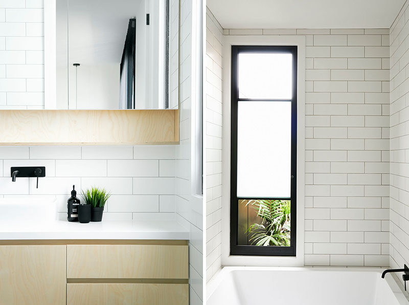 In this modern bathroom, simple white tiles cover the walls, while a built-in bathtub sits below the window, and the vanity features plywood and a white countertop. #ModernBathroom #WhiteBathroom