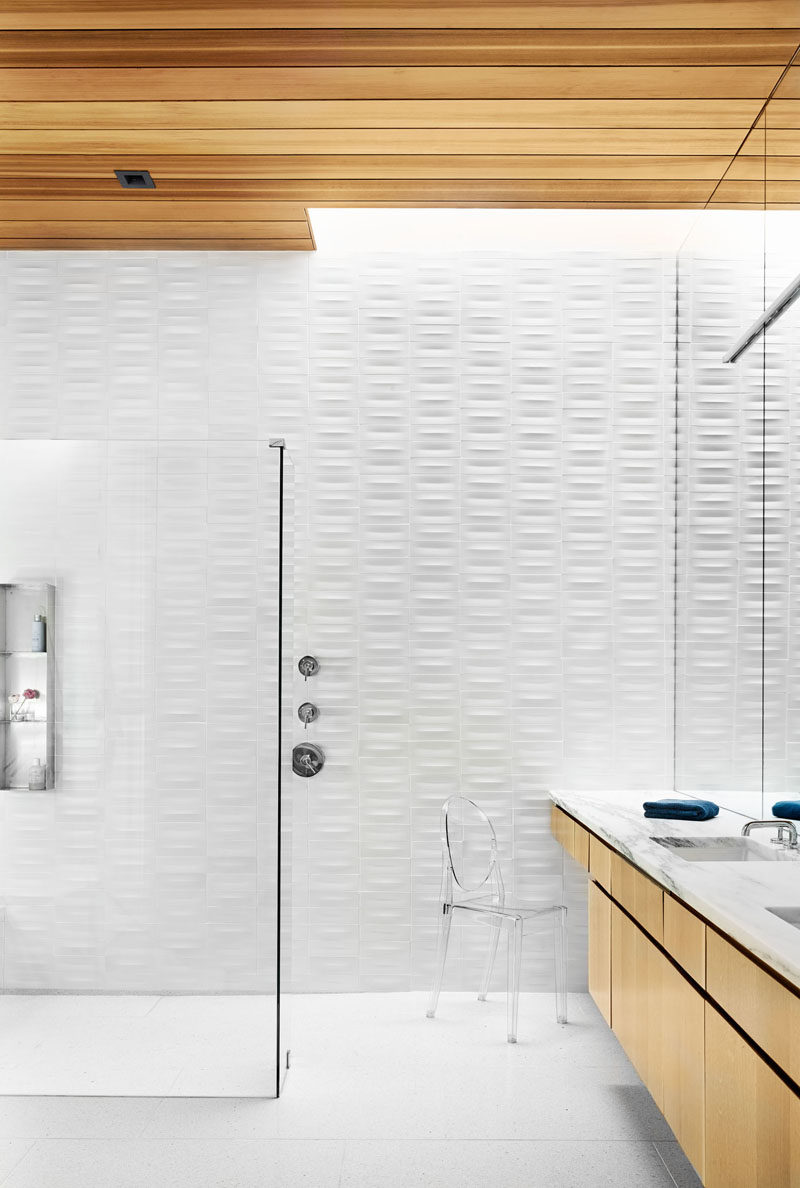 In this modern bathroom, textured white tiles cover the wall, while the wood cabinetry complements the wood ceiling. #Bathroom #WhiteAndWoodBathroom #BathroomDesign