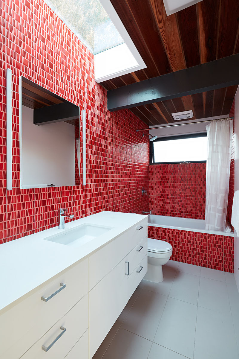 In this modern bathroom, bold bright red tiles cover the walls and bath surround, and contrast the white vanity. A skylight above the vanity helps to keep the room bright. #Bathroom #RedBathroom #BoldBathroom