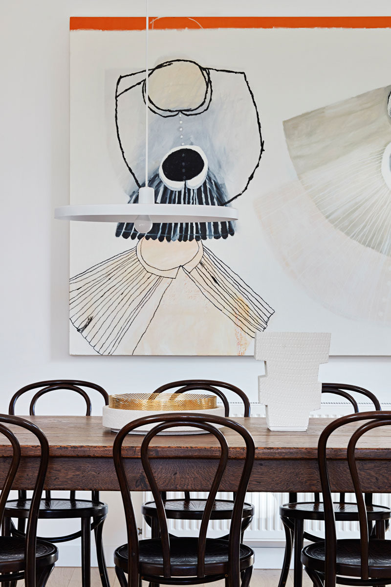 In this contemporary dining room, a large piece of art hangs on the wall, while a minimalist white pendant lamp hangs above the dark wood table and chairs. #DiningRoom