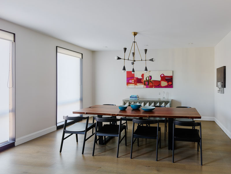 In this contemporary dining room, a large wood dining table sitting below a minimalist chandelier, and artwork on the walls. #DiningRoom