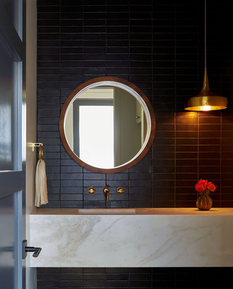 In this bathroom, dramatic dark subway tiles provide a strong contrast to the light-colored vanity and hanging pendant light. #ModernBathroom #DarkTiles