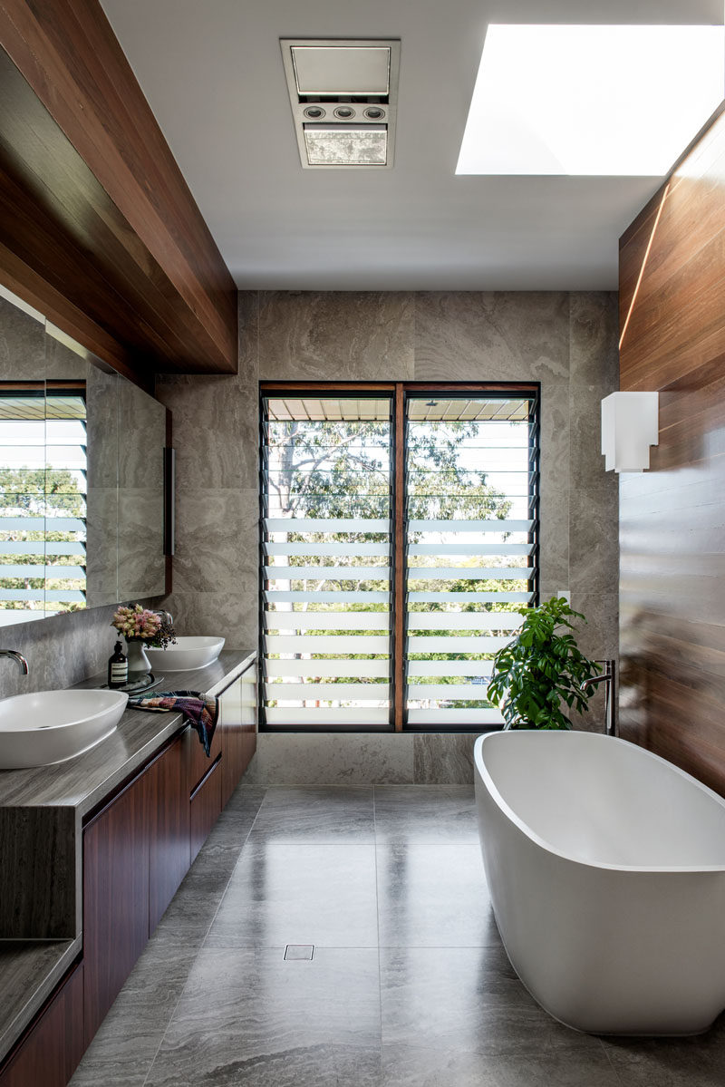 In this modern master bathroom, high ceilings create a sense of openness, while a skylight adds natural light to the bath area, and a large vanity mirror reflects the view outside. #MasterBathroom #BathroomDesign