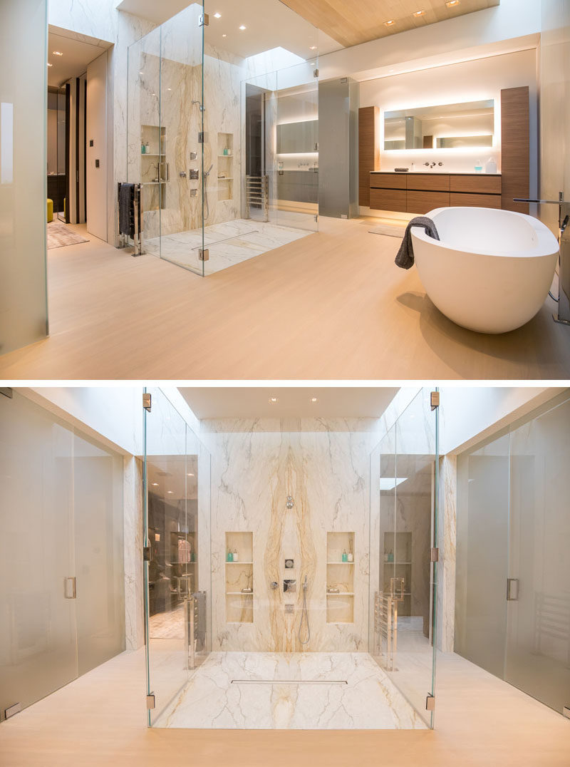 In this modern master bathroom, there's a large walk-in shower with a glass surround, while sitting adjacent to the shower is a freestanding bathtub, and a vanity with a back-lit mirror. #MasterBathroom #GlassEnclosedShower #BathroomDesign