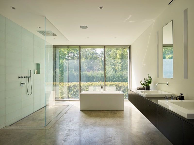 In this modern master bathroom, a large glass enclosed shower sits beside a freestanding bathtub, both of which can enjoy garden views. #ModernBathroom #BathroomDesign