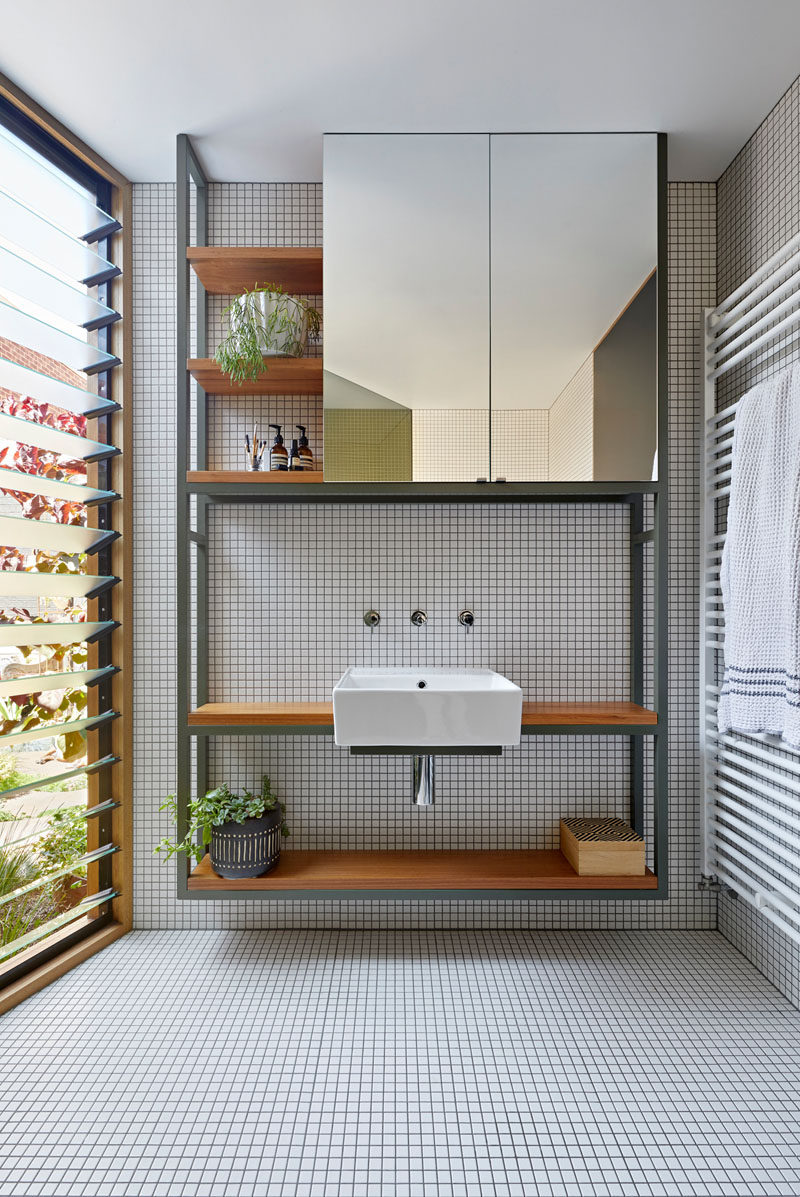 In this modern bathroom, a shelving unit with a mirror and wood shelves, sits beside louvre windows. #ModernBathroom #BathroomVanity