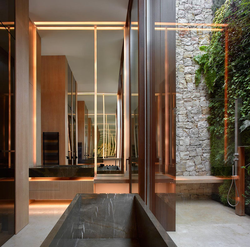 In this modern bathroom, a tall door opens to a private courtyard with a green wall and an outdoor shower. #Bathroom #ModernBathroom #OutdoorShower