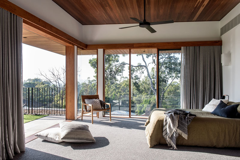 This modern master bedroom has floor-to-ceiling windows, and sliding doors that open up to a green roof overlooking the pool below. #MasterBedroom #Windows #WoodCeiling