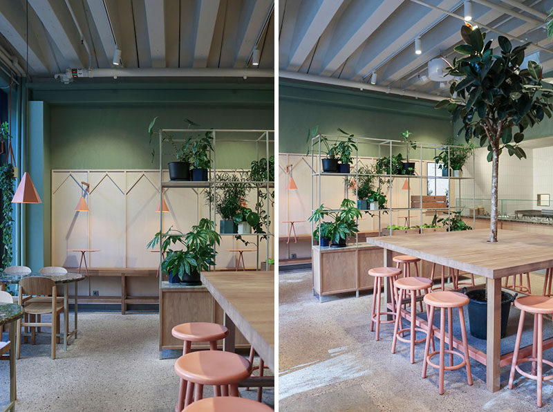 The community-style oak table features a tree at the centre of this restaurant, while open grid shelves are used to subdivide the space using green plants. #RestaurantInterior #InteriorDesign