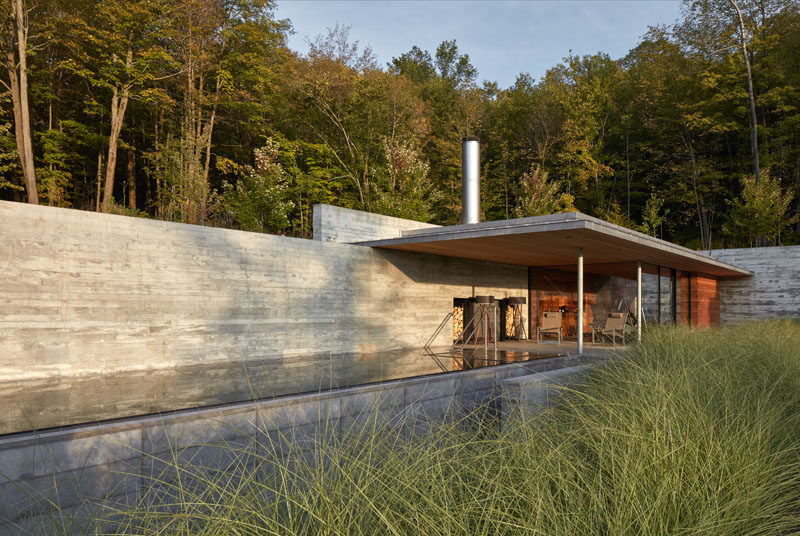 This modern concrete, wood, and glass pool house sits next to an infinity lap pool and hot tub, and features an outdoor fireplace, a gym, lounge, and changing areas. #PoolHouse #SwimmingPool #Architecture