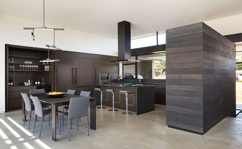 Inside this modern house, dark wood cabinetry has been used in the kitchen, while a minimalist light fixture hangs above the dining table. #DarkWoodKitchen #KitchenDesign #DiningRoom