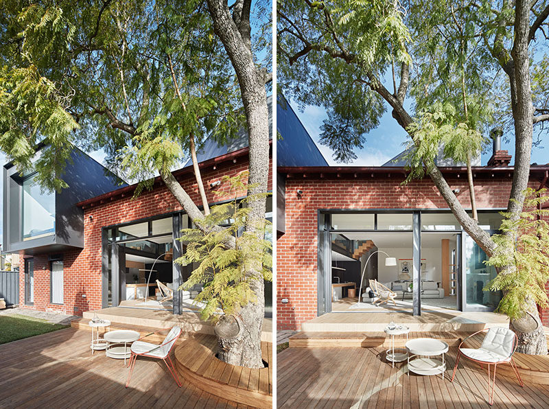 Sliding doors open the interior spaces of this renovated house to the backyard, that features a wood deck with seating that wraps around a large tree. #Backyard #Deck