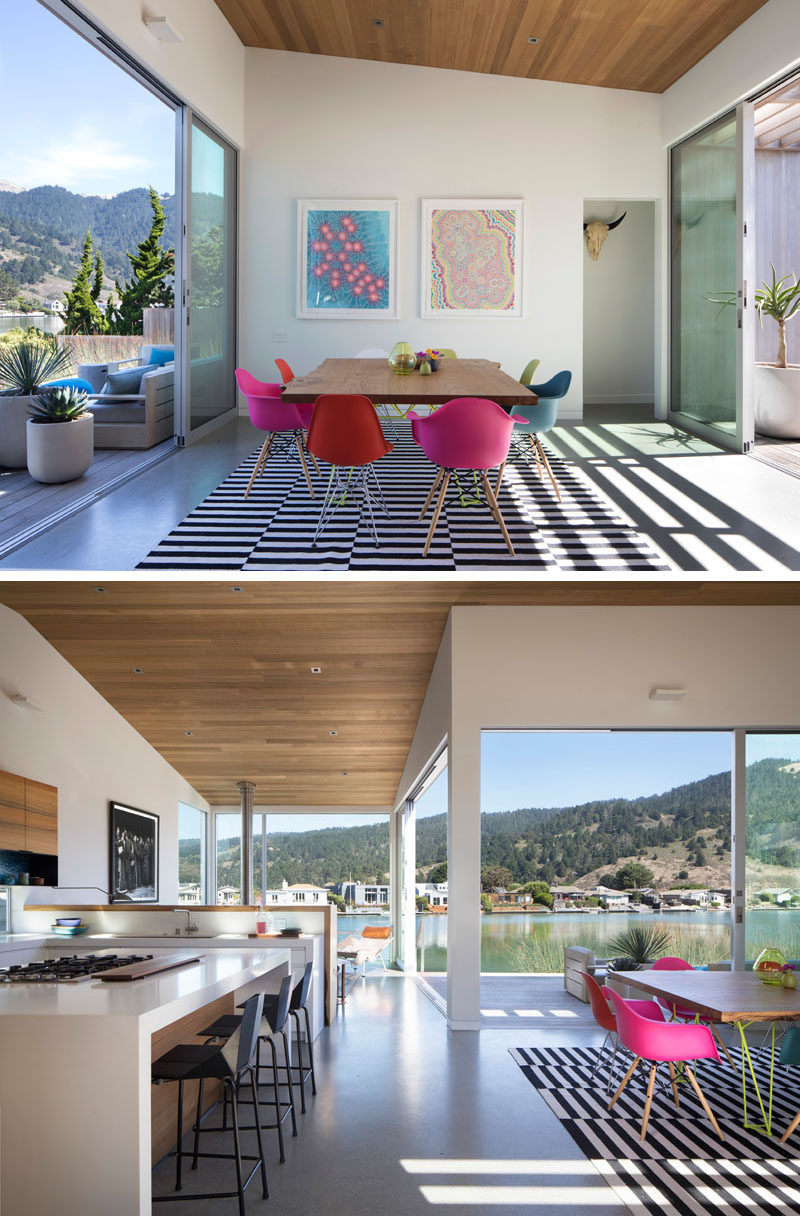 The sliding glass front door of this modern house opens up to the dining room, that has a sloped ceiling, and furnished with a square wood table and colorful chairs. #DiningRoom #Kitchen