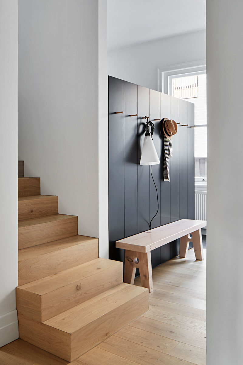 Stepping inside this home, there's a dark accent wall with hooks for hanging up jackets, and a wood bench for taking off shoes. #Entryway #InteriorDesign