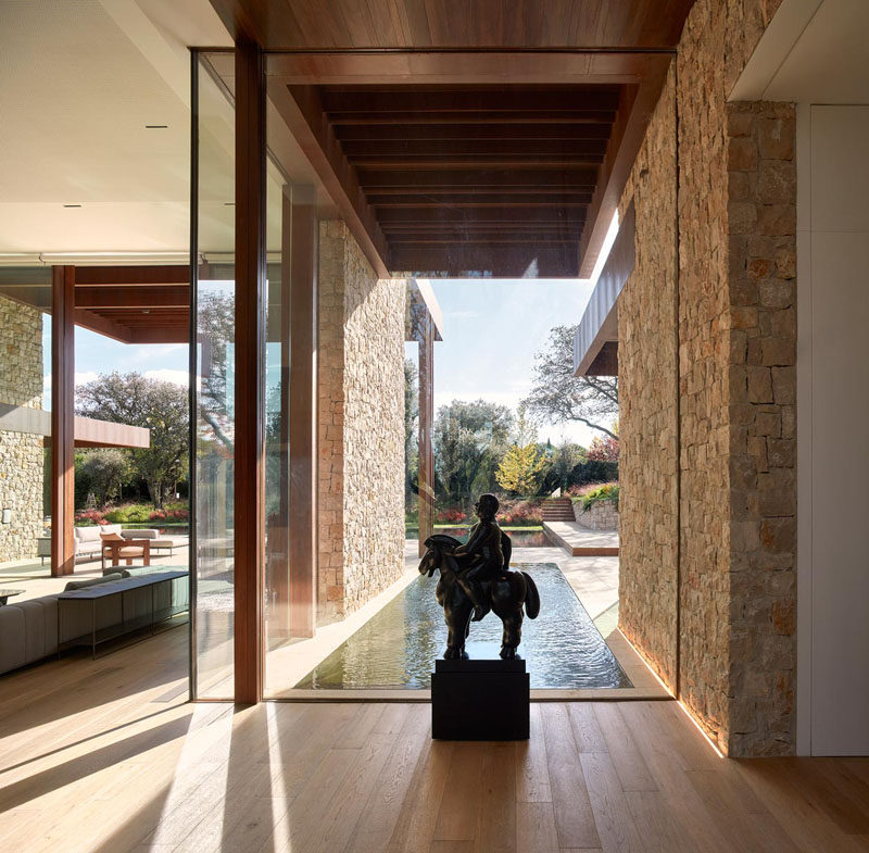 This glass wall provides a backdrop for a statue, and frames the water feature and garden outside. #GlassWall #WaterFeature