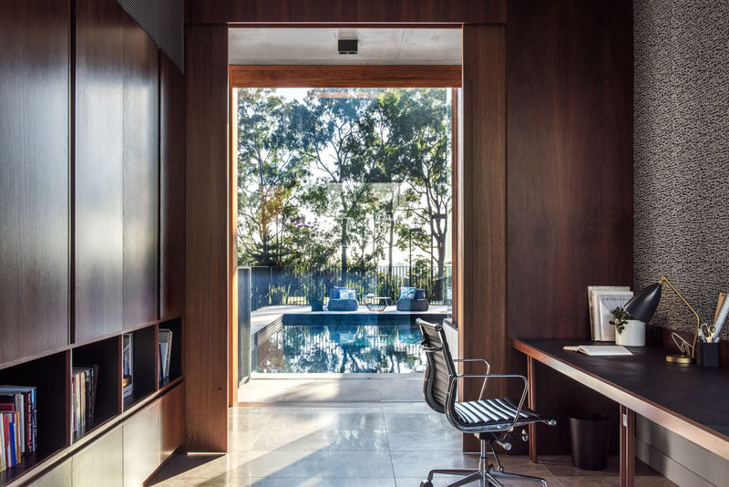 This modern home office features rich wood cabinetry and a view of the pool. #HomeOffice #Cabinets