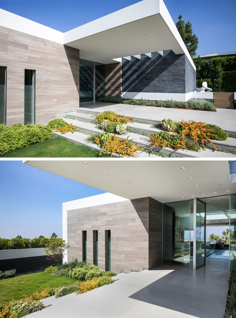 The dark-grey rough stacked-slate exterior of the house is capped with crisply contrasting white stucco, and a pivot-style all-glass front door and surround welcomes guests to this modern house. #Architecture #ModernHouse #GlassFrontDoor