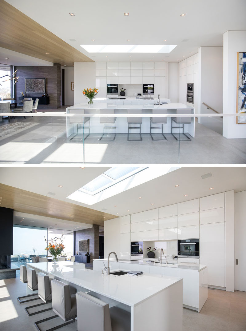 This modern house has sleek all-white kitchen islands and floor-to-ceiling cabinets that are minimalist in their design, with a skylight adding even more light to the bright space. #WhiteKitchen #ModernKitchen #KitchenDesign