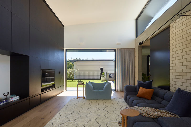 This modern living room has a black accent wall that surrounds the television, while a sliding glass door opens to the backyard. #LivingRoom #BlackAccentWall