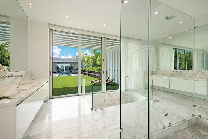 In this modern bathroom, a sunken bathtub is surrounded by Panish limestone, while large vanities and full-wall mirrors are featured on both sides of the room. #ModernBathroom #SunkenBathtub