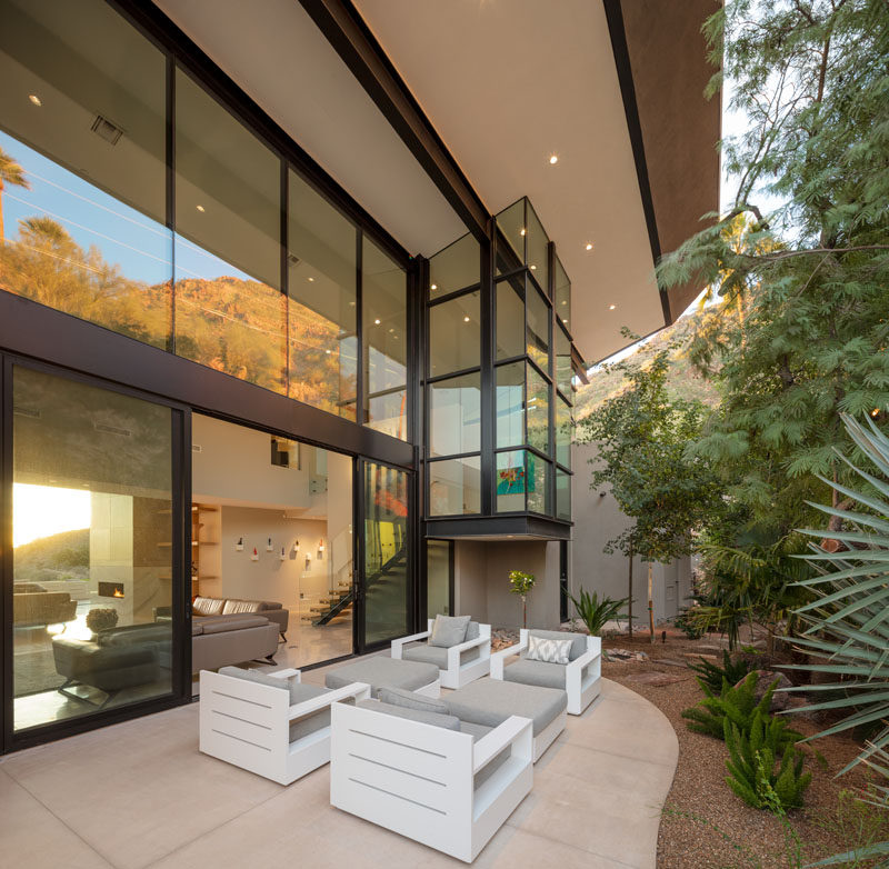 This modern house has a small patio that's located against the hillside, and is furnished with outdoor armchairs. #Patio #Landscaping #ModernHouse