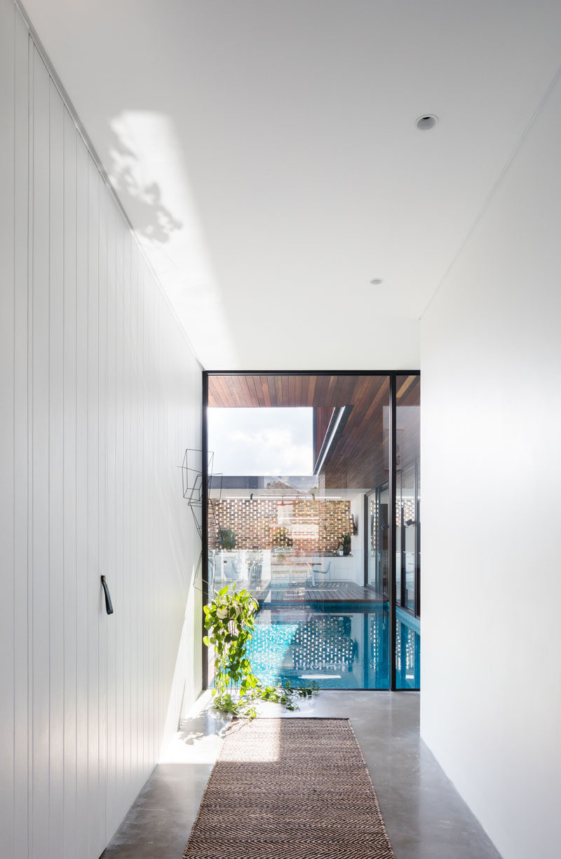 Inside this modern house, a hallway with bright white walls leads from the entryway towards the pool and social areas of the house. #InteriorDesign #Hallway #Windows