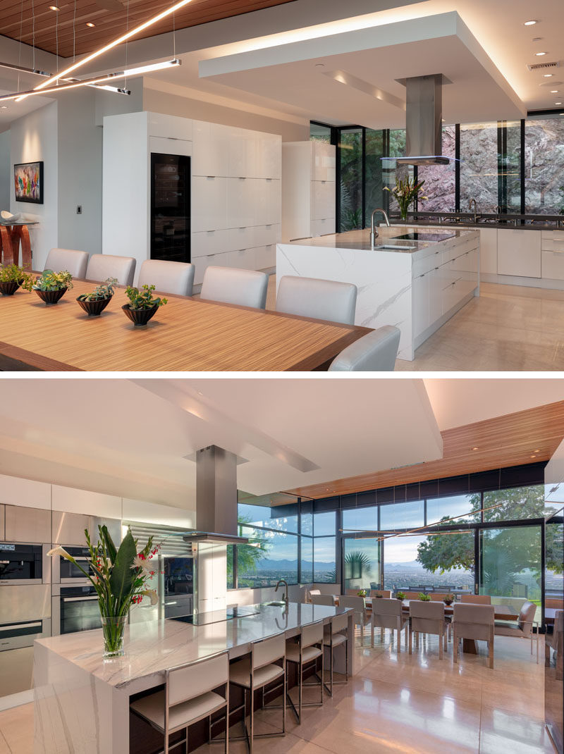 Behind the dining room in this modern house, is the mostly white kitchen. A central island increases the countertop area and provides a place for people to sit. #KitchenDesign #ModernKitchen