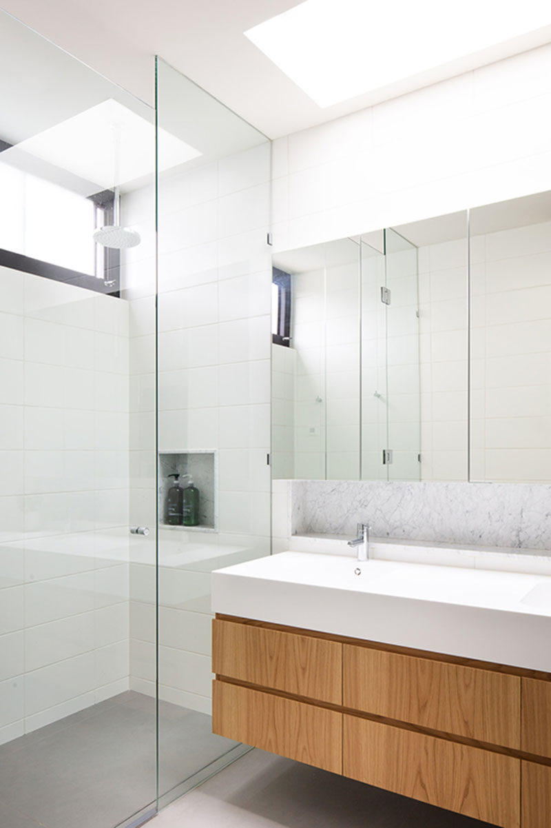 In this modern bathroom, a skylight helps to keep the white bathroom bright, while a wood vanity adds a natural touch. #ModernBathroom #BathroomDesign