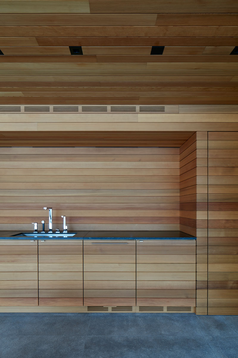 This modern pool house features a wood lined kitchen area with a dark grey countertop. #Kitchen #WoodKitchen #ModernKitchen