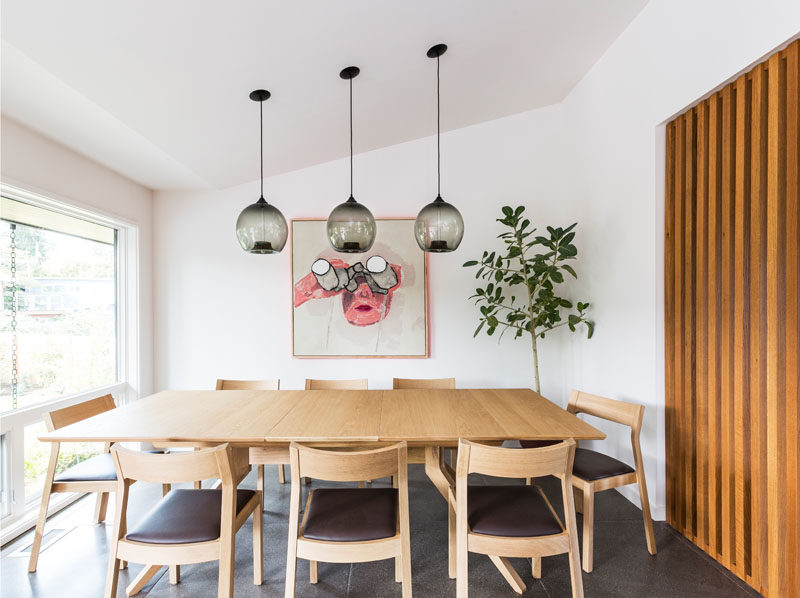 This modern dining room has three simple black glass pendant lights hanging above the table. A pop of color has been added to the wall in the form of a painting. #DiningRoom #ModernDiningRoom