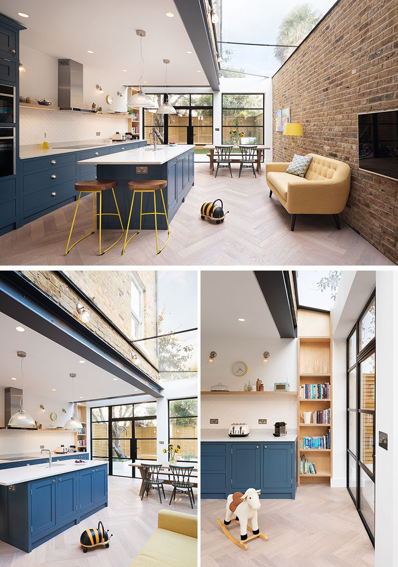 This modern extension is open plan with a new dark blue kitchen, a pastel yellow sofa that sits against a brick wall, and a dining area that has views of the backyard through the black-framed windows and doors. A skylight running the length of the extension adds an abundance of natural light to the space. #ModernHouseExtension #HouseExtension #BlueKitchen #Skylight