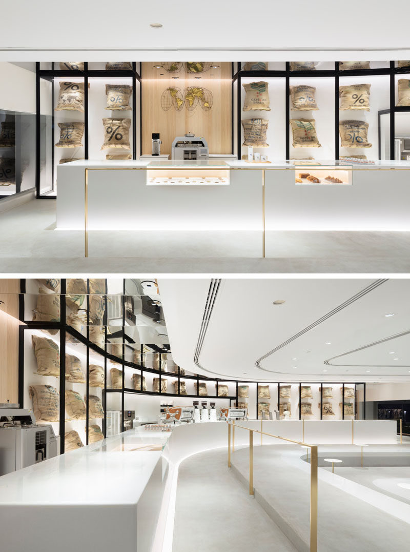 The design of this modern coffee shop has white coffee machines that almost disappear to the background in order to highlight the coffee beans presented in linen bags behind a glass case and the “beans map” element hanged next to it. #CoffeeShop #InteriorDesign