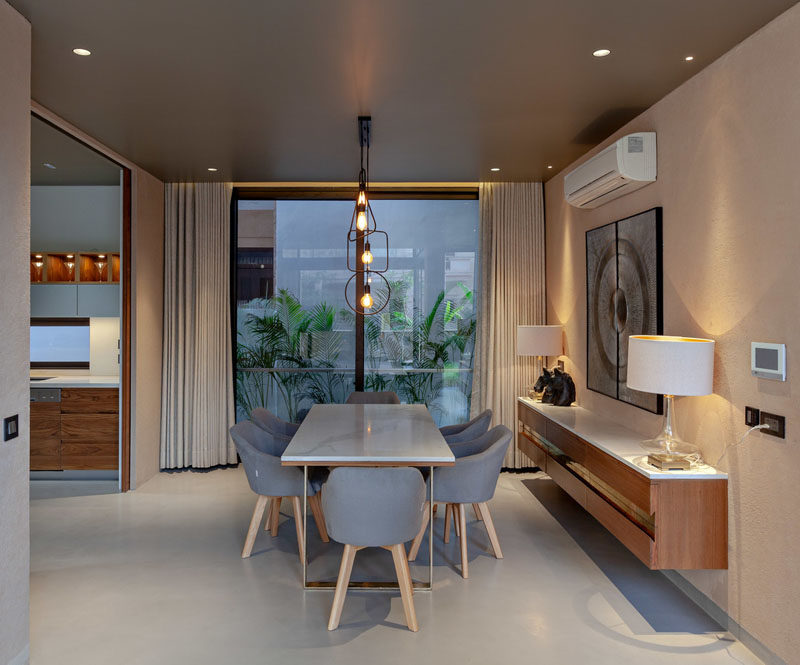 This modern dining room features minimalist lighting above the dining table, while a floating sideboard sits below artwork, and large windows provide a view of the plants outside. #DiningRoom