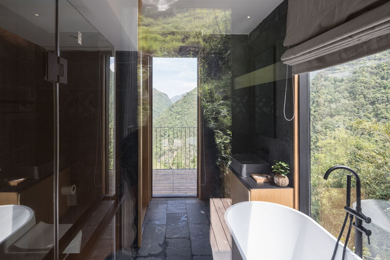 In this holiday cabin, the modern bathroom has a dark interior with a white freestanding bathtub positioned next to the window. #BathroomDesign #DarkBathroom #ModernBathroom