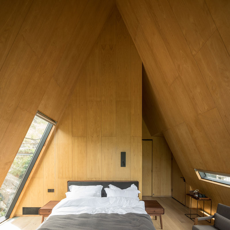 This interior of this modern cabin has wood panels covering the angled walls, while windows provide glimpses of the surrounded landscape. #ModernCabin #CabinInterior #Bedroom