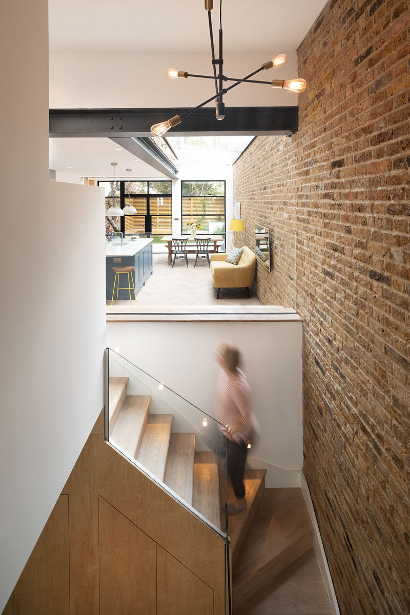 In this house, wood stairs connect the new extension to the basement downstairs, and from this angle, you can see the large metal beams that contrast the white walls and ceiling. #Stairs #HouseExtension #ModernInterior