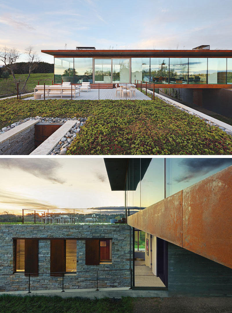 A large sliding door off the kitchen of this modern house leads out to a deck and green roof. Below the green roof is the lower volume of the house that uses stone and eventually plantings/vines to blend with the ground. #ModernHouse #Deck #GreenRoof